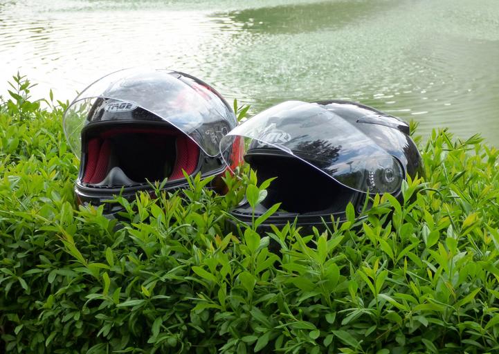 Dve čierne prilby na motorku položené vo vysokej tráve