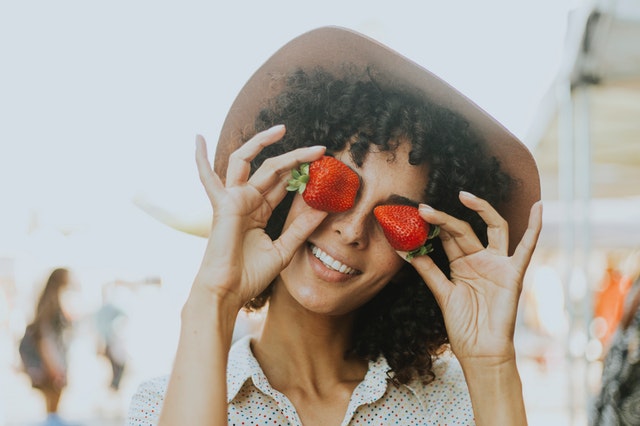 Usmiata žena v klobúku drží pred očami jahody